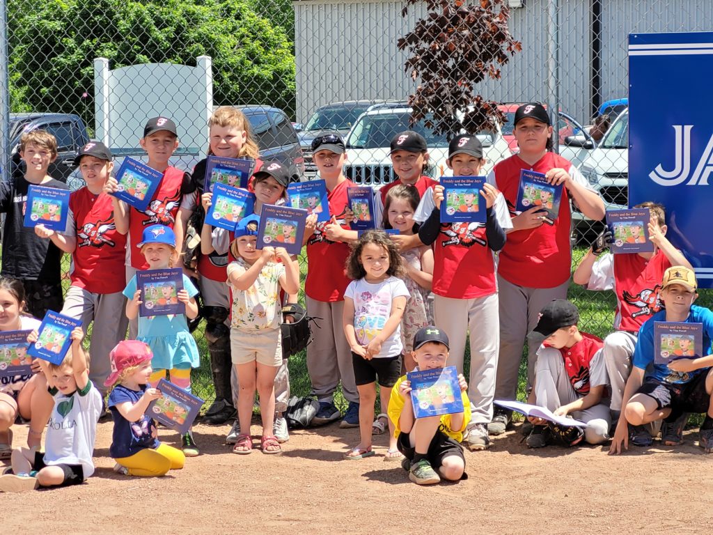 Group of children at baseball game holding up copy of Blue Jays book
